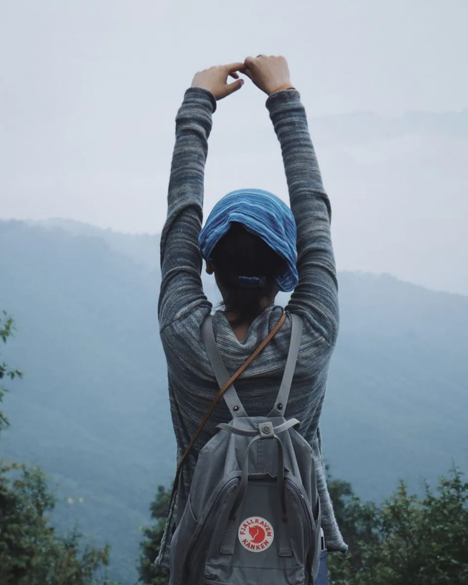 A woman trekker stretching while facing Nepal's misty mountains